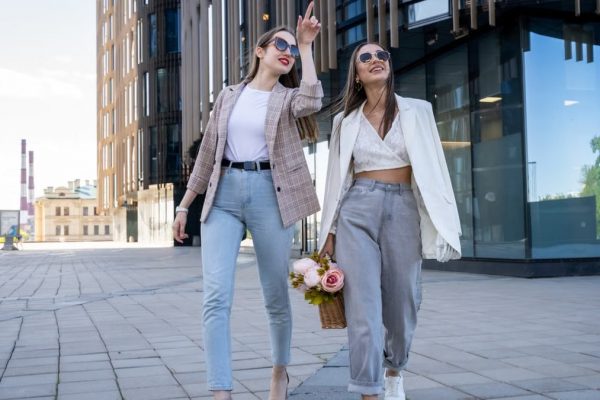 Two stylish women in sunglasses walking outdoors, embracing fashion trends.